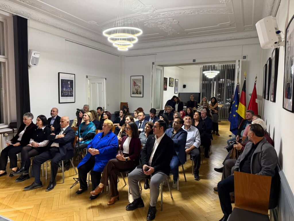 Zahlreiche Gäste sitzen in Stuhlreihen im Saal der TDU am Kurfürstendamm, an der Seite die Flaggen Deutschlands, der Türkei und der Europäischen Union