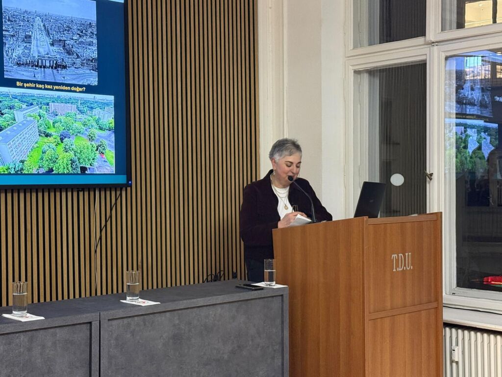Dr. Nejla Kılınç spricht am Rednerpult mit der Aufschrift TDU, links eine Leinwand mit historischen und heutigen Stadtansichten