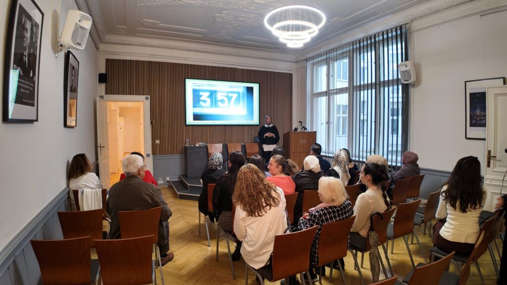 Teilnehmende sitzen im Saal der TDU am Kurfürstendamm und verfolgen den Workshop, vorne eine Leinwand und das Rednerpult